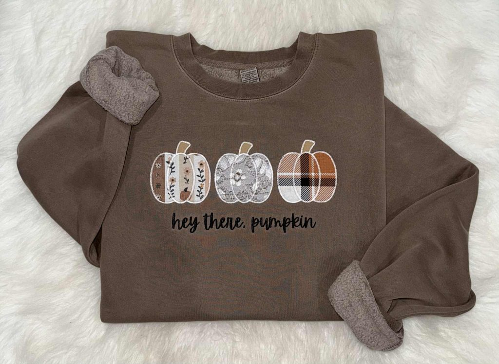 Brown crewneck sweatshirt embroidered with three fall pumpkins and 'hey there, pumpkin' in script lettering